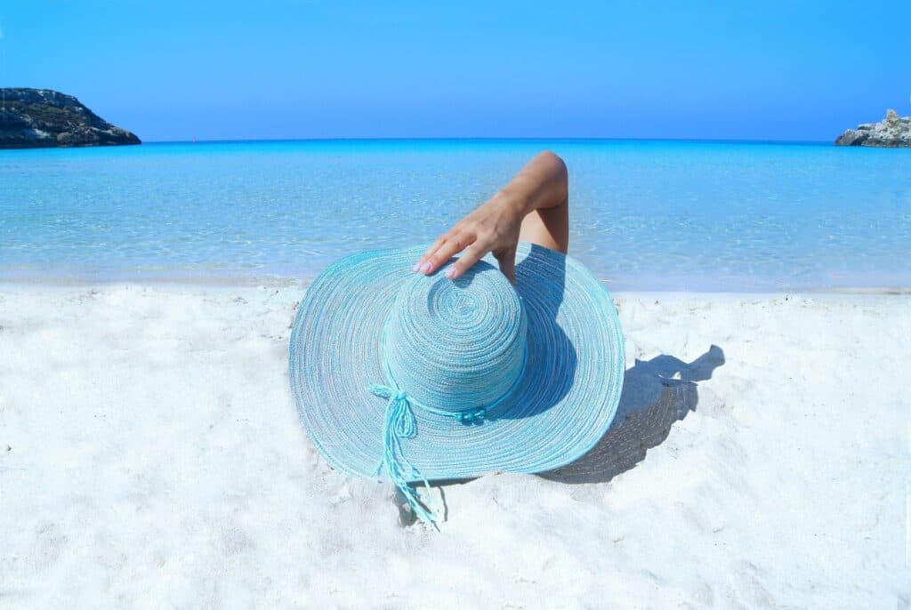 woman with a blue hat laying on the sand watching the sea